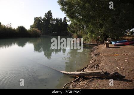 L'Asi, piccolo ruscello che scorre tra alberi di eucalipto, barche e un molo sulla sua riva e un thicket nella Valle delle sorgenti, Valle di Beit She'an. Foto Stock
