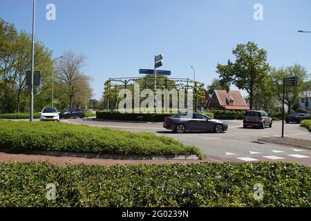 Rotonda nel villaggio olandese di Bergen con siepe edera, alberi di spalliera e segno posto. Auto e ciclista. Primavera, Paesi Bassi, maggio Foto Stock