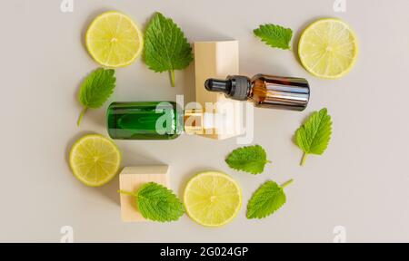 Siero con vitamina C. olio essenziale di limone. Bottiglia di vetro marrone e verde con pipetta, fette di limone con foglie di menta su fondo grigio. Salute Foto Stock