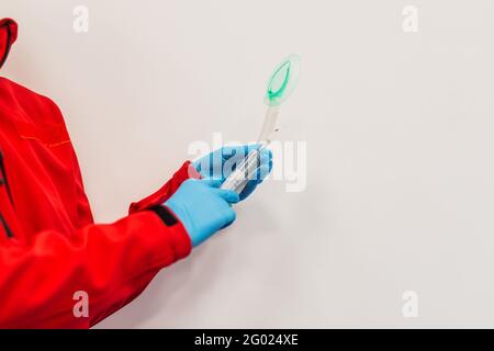 Un medico in una uniforme rossa tiene l'apparecchiatura di intubazione, vicino - in su, uno sfondo bianco. Pronto soccorso Foto Stock