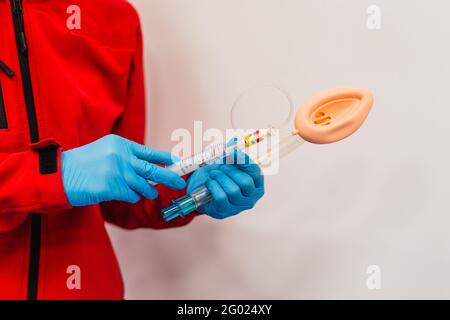 Un medico in una uniforme rossa tiene l'apparecchiatura di intubazione, vicino - in su, uno sfondo bianco. Pronto soccorso Foto Stock