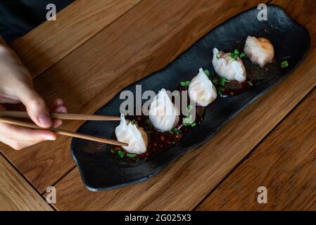 Chiudi la mano femminile con gnocchi cinesi caldi. Dimsum cinese al vapore con bastoncini. Vista dall'alto. Foto Stock