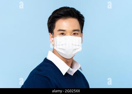 Primo piano ritratto di giovane bell'uomo asiatico che indossa un medico maschera facciale isolata su sfondo azzurro Foto Stock