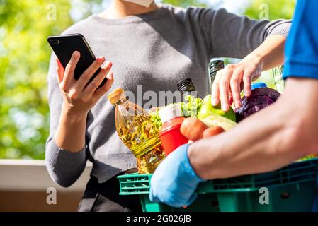 Donna cliente che controlla i generi alimentari che ha ordinato online e consegnato da deliveryman a casa, servizio di consegna di cibo nel momento del concetto pandemico Foto Stock