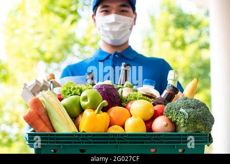 Il deliveryman asiatico indossa la maschera facciale tenendo il cestino della drogheria all'aperto, servizio di consegna di cibo igienico nel tempo del concetto pandemico Foto Stock