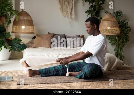 giovane africano seduto in janushirshasana seduta in avanti piega postura a casa Foto Stock