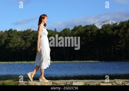 Vista laterale ritratto di una donna in bianco dres Walking in un lago in montagna Foto Stock