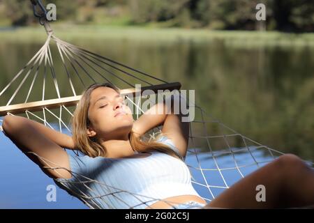 Donna rilassata che riposa in un'amaca in un lago in montagna Foto Stock