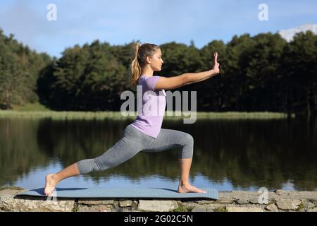 Vista laterale ritratto a corpo pieno di una donna che pratica il tai chi posa in un lago Foto Stock