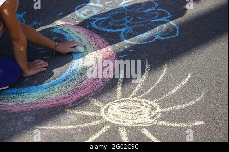 Carino bambino disegna il sole con gesso all'aperto, in estate, gesso. Messa a fuoco selettiva. Foto Stock