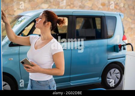 Una donna riempie la sua auto con benzina ad una stazione di benzina self-service e paga con una carta di credito ad una macchina Foto Stock