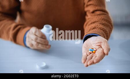 primo piano di vista della giara della medicina e pillole multicolore in mani di anziani su sfondo grigio Foto Stock