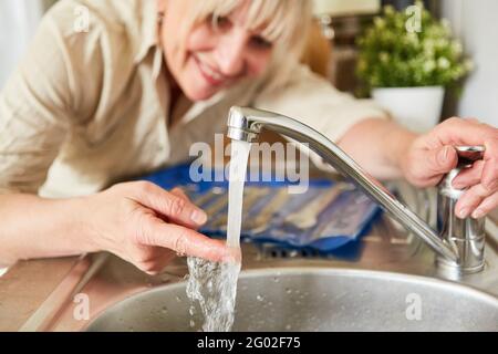 La donna di handyman controlla il rubinetto del miscelatore per l'acqua calda sul lavandino in cucina Foto Stock