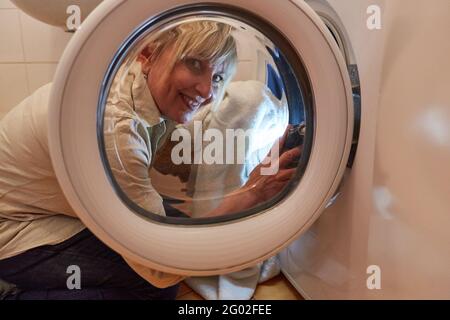 Donna sorridente come una casalinga riempie l'asciugatrice o lavatrice Foto Stock