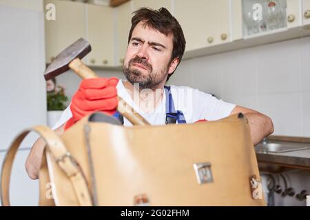 Fai-da-te-tuo o artigiano guarda scetticamente a un martello nel suo borsa portautensili Foto Stock