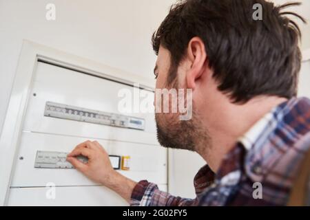 L'elettricista controlla l'interruttore dell'impianto elettrico nella distribuzione scatola Foto Stock