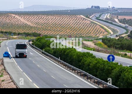 Autocisterna con targhe di merci pericolose circolanti in autostrada, una strada che si perde in background tra oliveti. Foto Stock