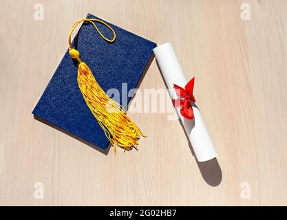 Tassello giallo da tappo graduato, diploma blu e rotolo di carta legato con nastro rosso con prua su sfondo di legno beige, piatto, vista dall'alto, mortarb Foto Stock