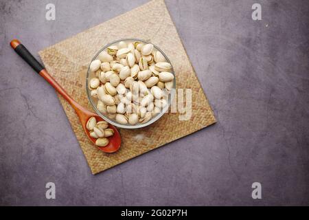 pistacchi noci in ciotola e cucchiaio di legno nero sfondo Foto Stock