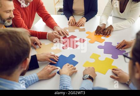 Gruppo multietnico diversificato di persone che collaborano alla composizione di pezzi di puzzle insieme Foto Stock