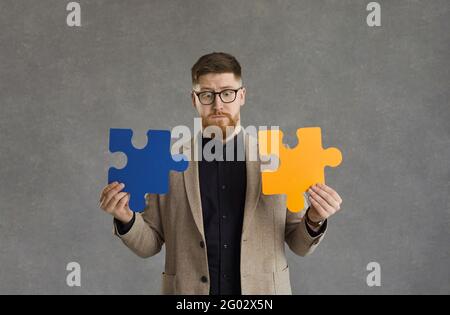 Uomo confuso cercando di collegare due pezzi di puzzle come metafora per la risoluzione dei problemi Foto Stock