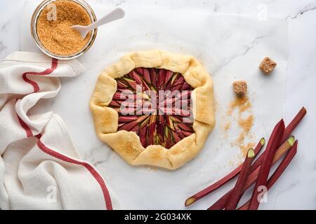 Galette con rabarbaro fresco processo di preparazione e ingredienti farina, acqua, burro, zucchero e rabarbaro per la cottura su fondo di marmo bianco. Chris Foto Stock