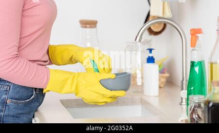 Piatti di lavaggio donna irriconoscibili, indossando guanti di gomma Foto Stock