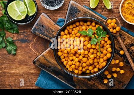 Ceci fritti con curcuma in piastra di ceramica su un vecchio tavolo di legno sullo sfondo. Ceci piccanti arrosto o chana Indiana o Chole, popolari spuntini reci Foto Stock