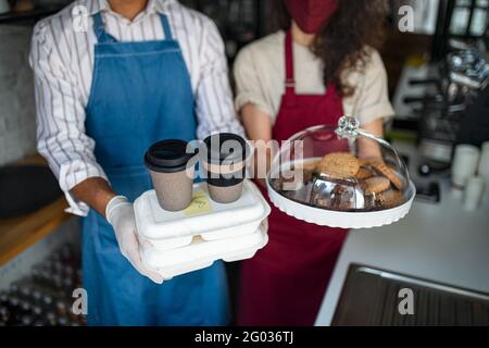 Camerieri irriconoscibili che preparano un ordine di take away, guardando la macchina fotografica. Concetto di coronavirus. Foto Stock