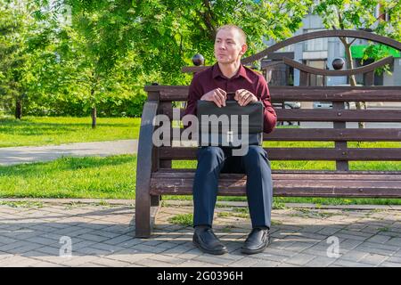 Il lavoratore in ufficio in un tuta da lavoro e con una valigia si siede con una vista sciocca sulla panca Foto Stock