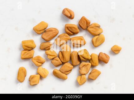 diversi semi di fenugreek intero si avvicinano su una piastra di ceramica grigia Foto Stock