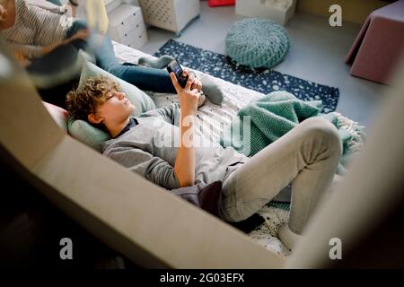 Ragazzo sdraiato sul letto con lo smartphone Foto Stock
