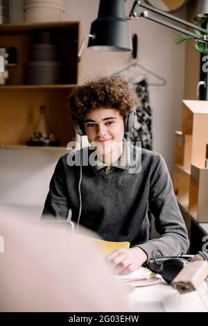 Ritratto di un ragazzo sorridente riccamente che indossa le cuffie seduto alla scrivania Foto Stock