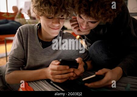Sorridi i fratelli che condividono lo smartphone mentre sono seduti in salotto a casa Foto Stock
