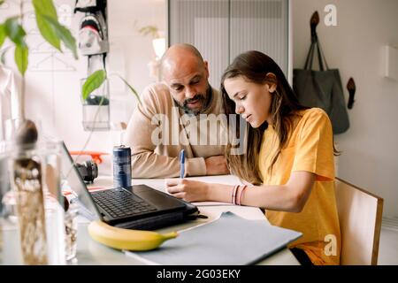 Padre che assiste la figlia facendo i compiti a casa Foto Stock