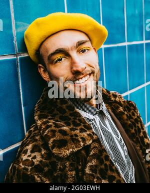 Ritratto di un giovane sorridente che indossa una berta gialla contro una parete piastrellata blu Foto Stock