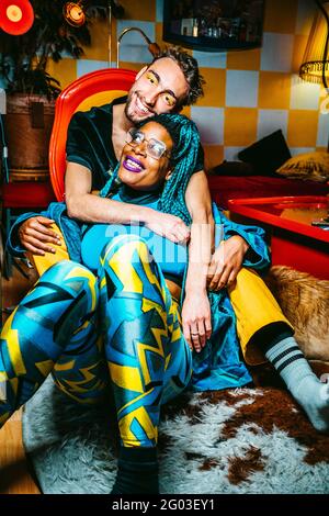 Ritratto di un giovane sorridente che abbracciava un amico hipster femminile mentre si siede in soggiorno Foto Stock