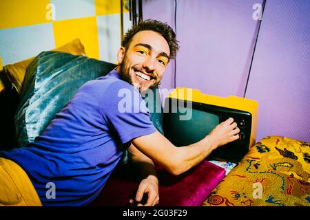 Ritratto di felice giovane uomo con televisore vecchio stile sdraiato sul divano in soggiorno Foto Stock