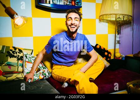 Ritratto di giovane allegro seduto sul divano in soggiorno Foto Stock