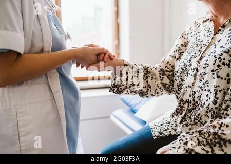 Sezione centrale del medico femminile che tiene la mano del paziente anziano alla clinica medica Foto Stock
