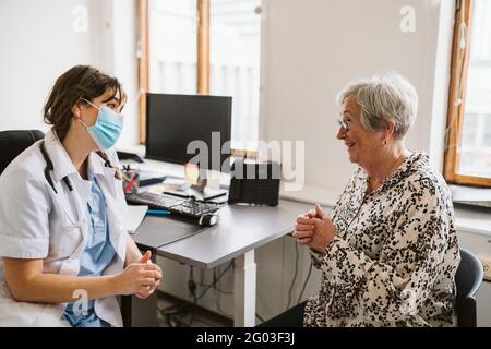 Sorridente paziente senior che parla con un medico esperto indossando maschera facciale Foto Stock
