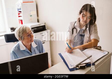 Infermiera femminile anziana che guarda la prescrizione di scrittura del medico alla clinica medica Foto Stock