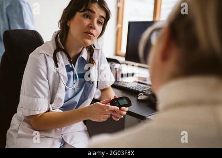 Medico femminile che spiega glaucometer mentre parla con il paziente in clinica medica Foto Stock