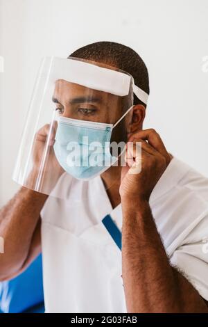 Medico di sesso maschile indossando maschera protettiva e visiera protettiva durante COVID-19 Foto Stock