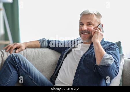 Vista laterale di un uomo anziano sorridente che ha una conversazione telefonica Foto Stock