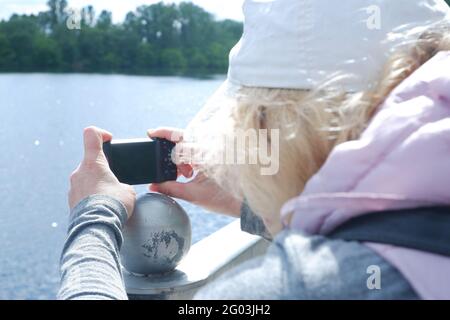 Una ragazza con cappuccio bianco scatta foto del paesaggio acquatico con una macchina fotografica. Giornata di San Veronica Giornata del fotografo . Foto Stock