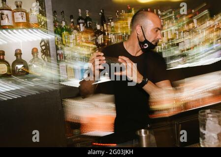 Barcellona, Spagna - 28 maggio 2021: Un giovane barman crea cocktail dietro il bar, muovendosi e facendo cocktail all'interno del nightclub Foto Stock