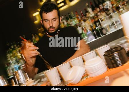 Barcellona, Spagna - 28 maggio 2021: Un giovane barman crea cocktail dietro il bar, muovendosi e facendo cocktail all'interno del nightclub Foto Stock