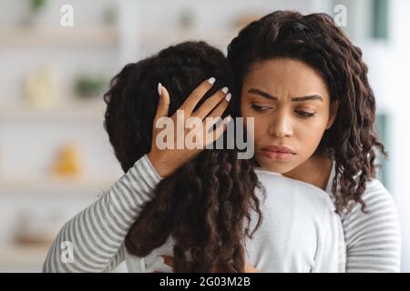 Preoccupata giovane madre nera che conforta la sua figlia piangente Foto Stock