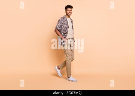 Foto del profilo del corpo di una persona di pelle scura e allegra che cammina guarda la fotocamera isolata su sfondo di colore beige Foto Stock